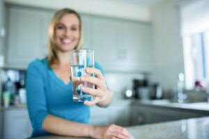 Woman holding out a clear glass of water in her kitchen. 