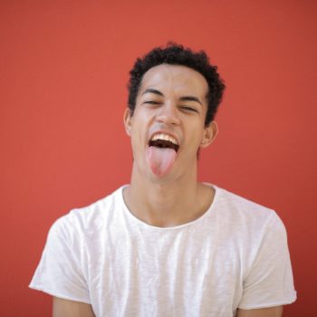 Man sticking his tongue out against a red background. Learn about the nuances of oral thrush.