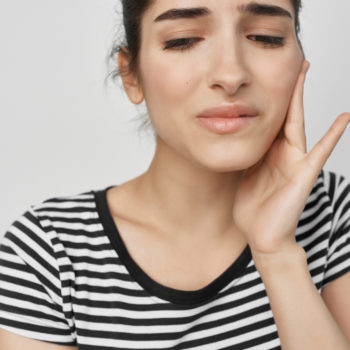 young woman with finger on her lips indicating tooth pain.