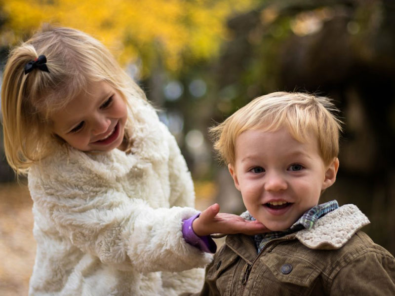 Young, toddler-aged sister and her brother smiling at camera.
