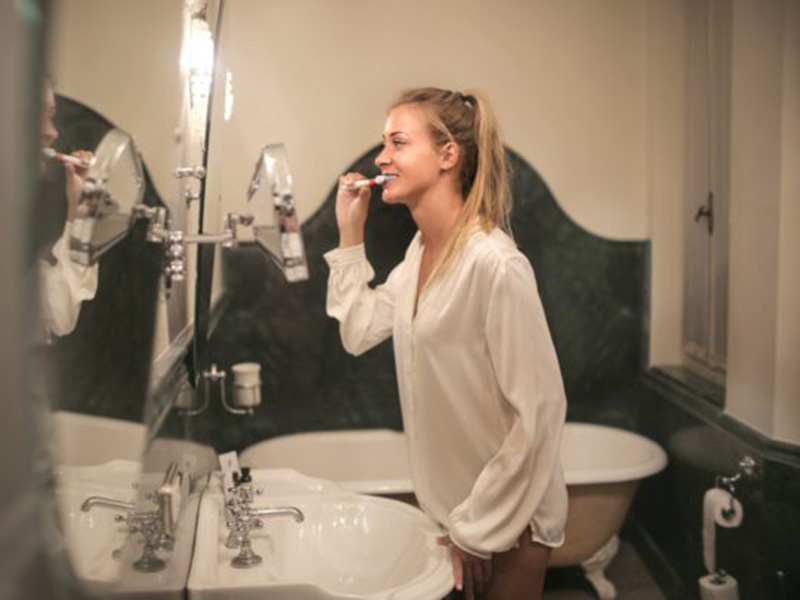 Woman brushing her teeth in the mirror.